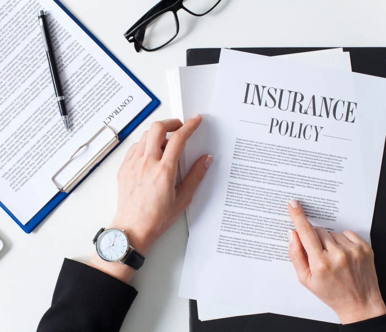 Hands reviewing insurance policy and contract documents.